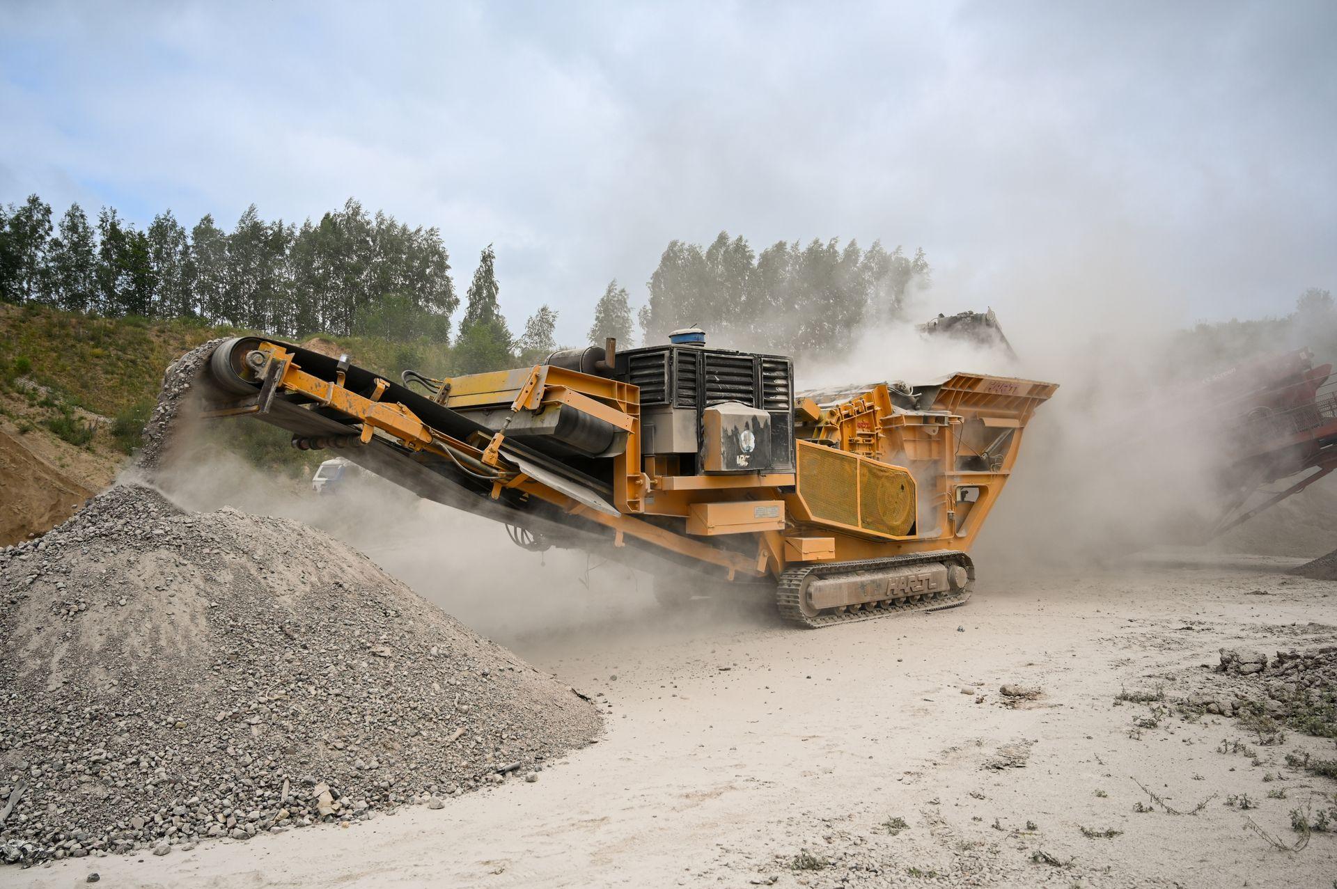 Tracked crushing plant discharging onto a stockpile, dust rising off the conveyor