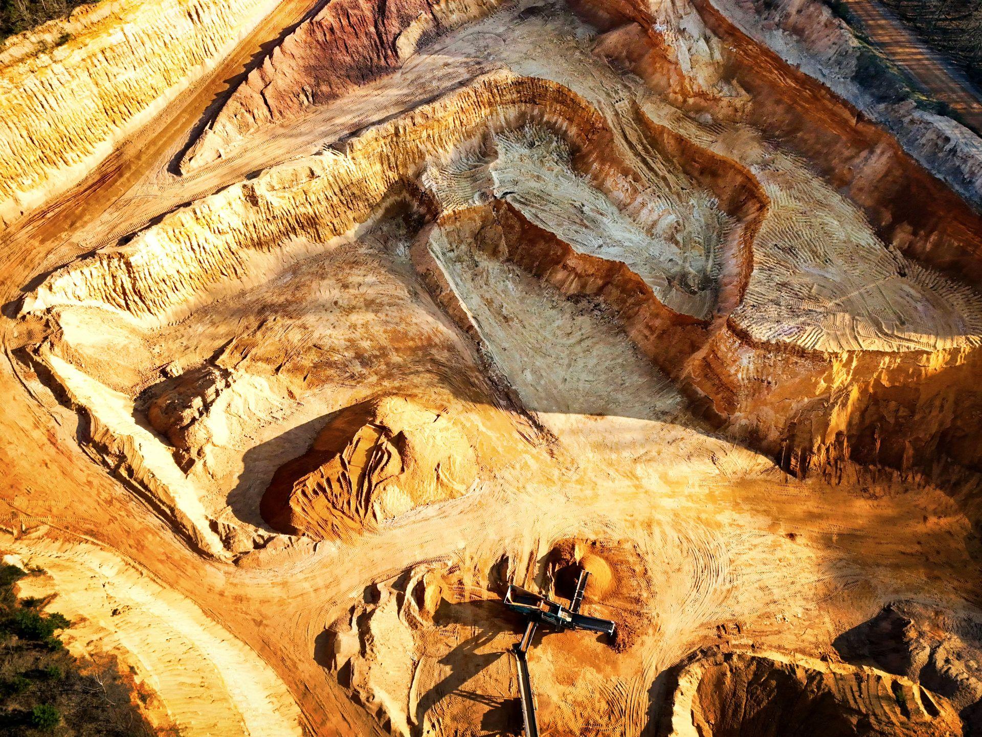 Aerial view of a benched open-pit sand working, warm ochre faces and haul roads cut into the deposit