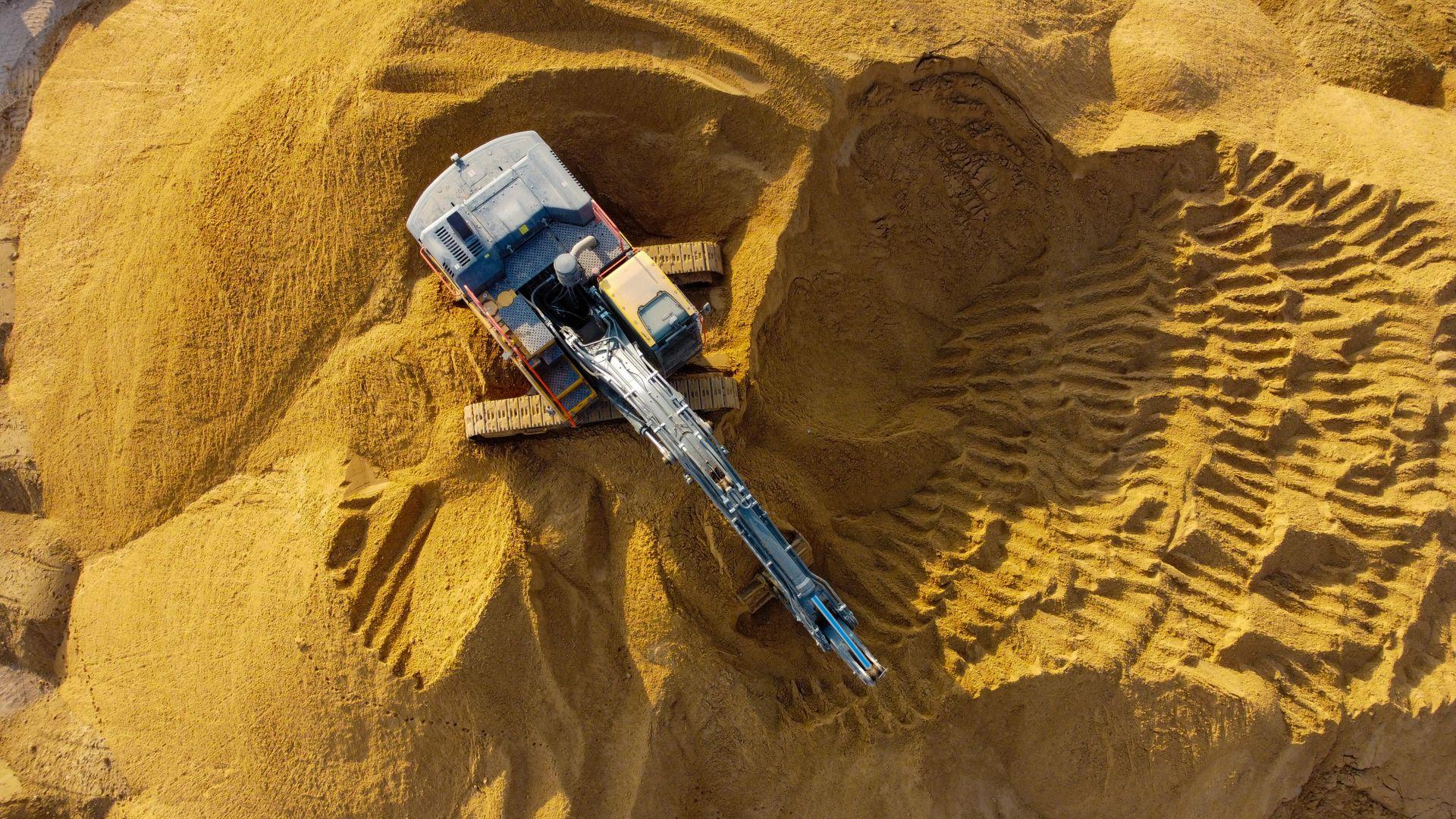 Overhead view of a tracked excavator working a face of silica sand